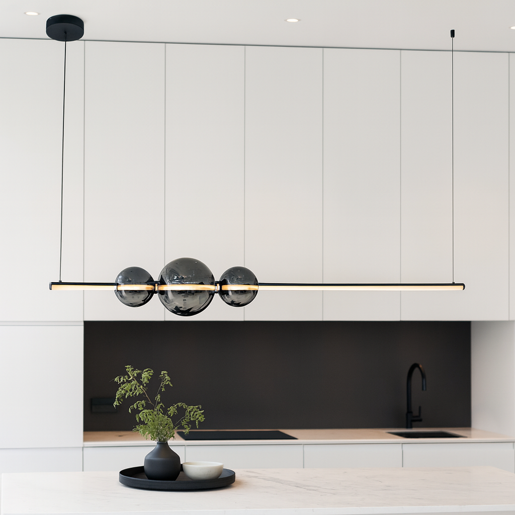 Modern kitchen with 120cm linear pendant light featuring smoked glass globes, suspended above a large island with neutral cabinets and black accents.